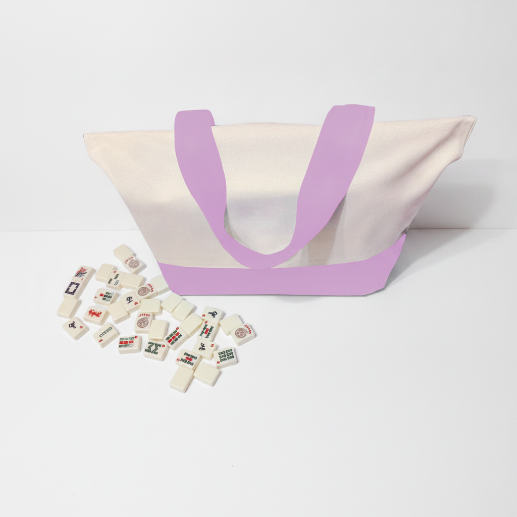 A canvas tote bag with a cream body, lavender purple handles and base trim, shown on a white studio background with several small white game pieces scattered in front.