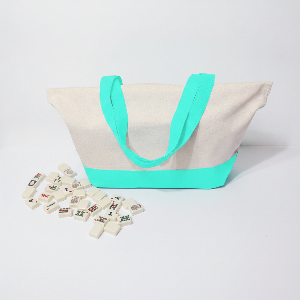 A canvas tote bag with a natural off-white body, bright mint handles and base trim, shown on a light gray studio background with small decorative tiles scattered in front.