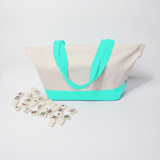 A canvas tote bag with a natural off-white body, bright mint handles and base trim, shown on a light gray studio background with small decorative tiles scattered in front.
