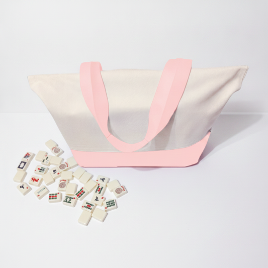 White canvas  tote bag with pink handles and scattered domino pieces on a light gray background